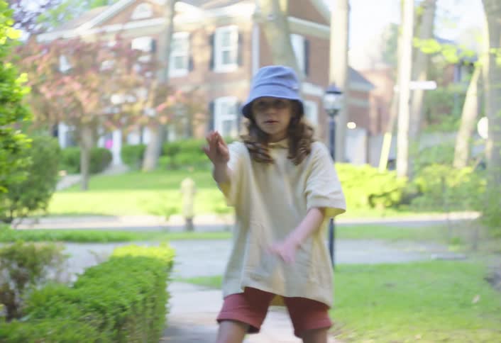 A child wearing a blue bucket hat and a lightcolored shirt crouched down on a paved pathway next to a wellmaintained hedge the child is focused on something on the ground possibly rocks or plants and appears to be playing or observing