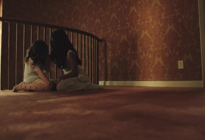 Older girl comforts a younger girl while they both kneel near interior railing