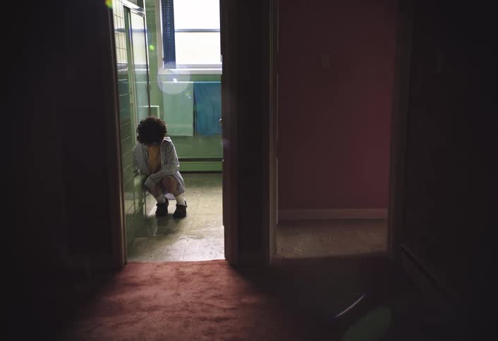 A sad boy kneels next to a shower reaching for something inside