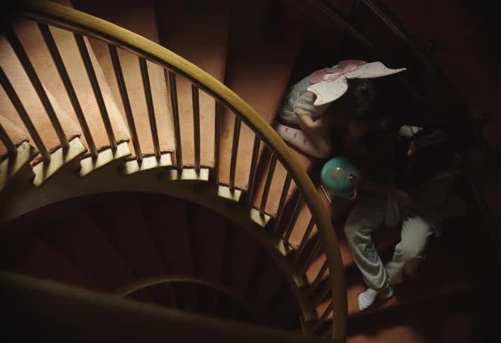 Two girls one of them wearing a pair of fairy wings sit on a spiral staircase and spin a globe atlas