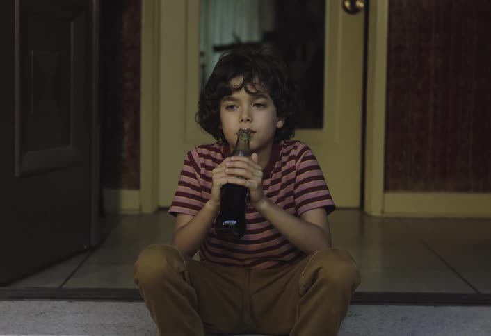 Boy sitting drinking soda from a glass bottle