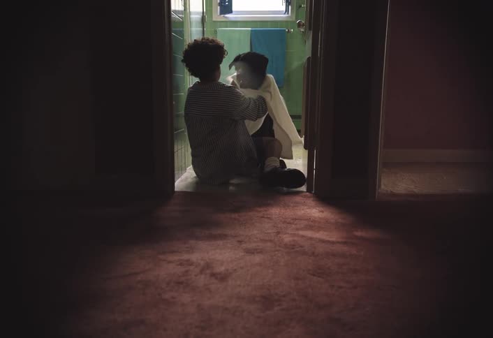 Boy sitting in bathroom doorway and drying a dog