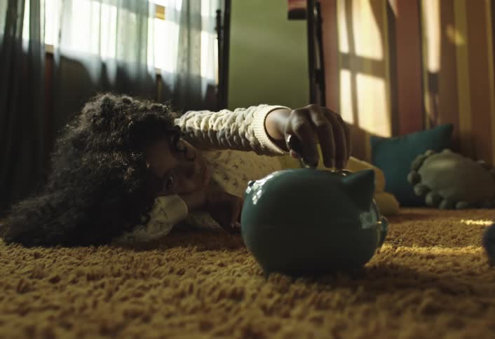 Girl lying on the carpet putting a coin into a piggy bank