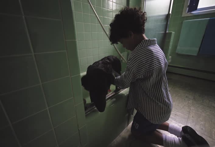 Boy kneeling next to a bathtub giving a dog a bath