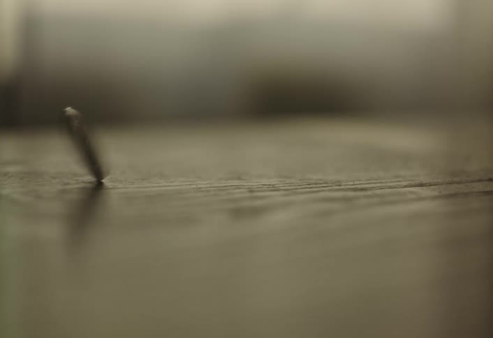A small dark cylindrical object possibly a nail or a similar piece of hardware spinning on a flat surface it starts upright wobbles and then gradually slows down and lays flat