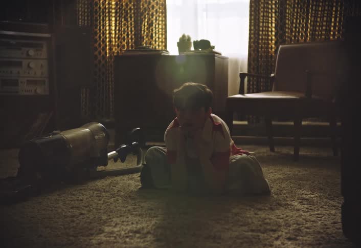 Boy sitting cross legged on the living room floor leans forward onto his elbows