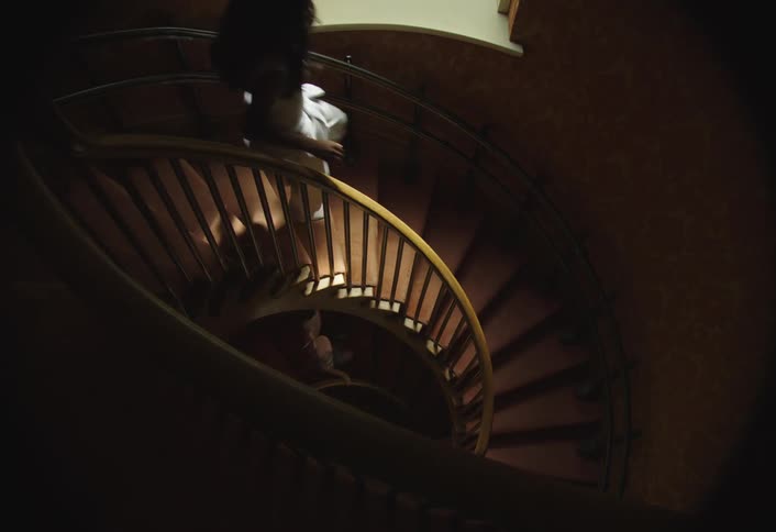 Two girls run down a winding staircase inside of a building