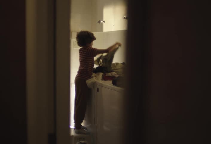 Male teenager sorts laundry clothing while standing in a laundry room indoors during daytime