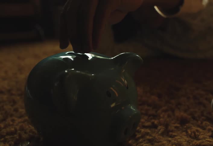 Close up of a teenage girl dropping coins into a green ceramic piggy bank