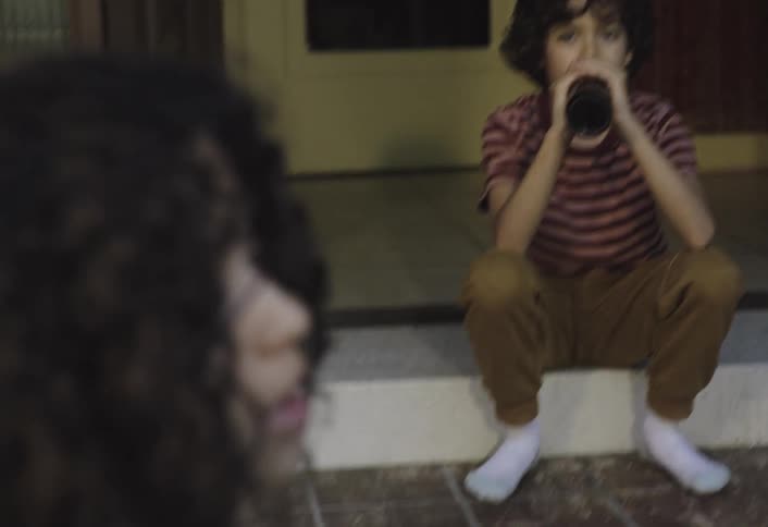 Two children sitting with one of them drinking from a bottle