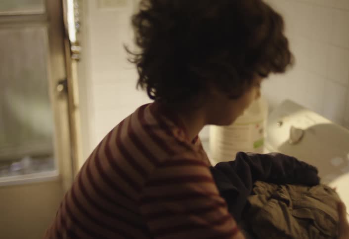 Boy holding clothes on top of a washing machine