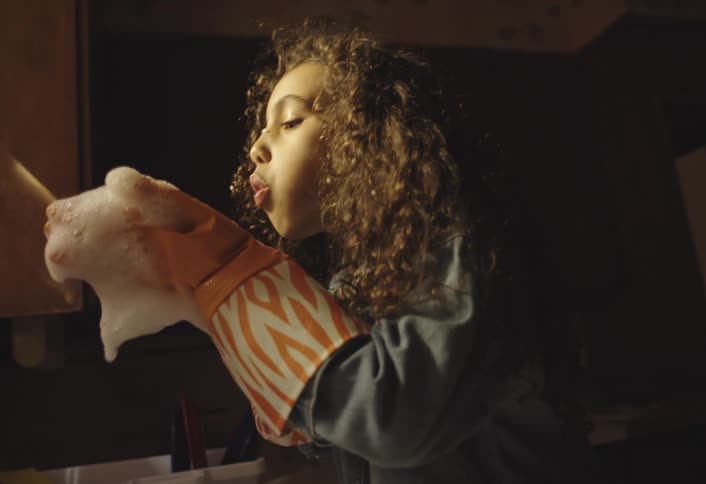 Teenage girl washing dishes in the kitchen picks up foam and blows on it