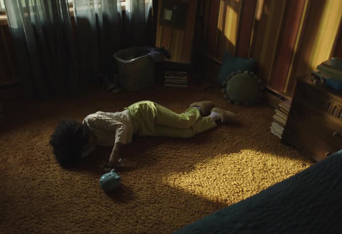 Curly haired girl lying in her room and putting coins into a piggy bank