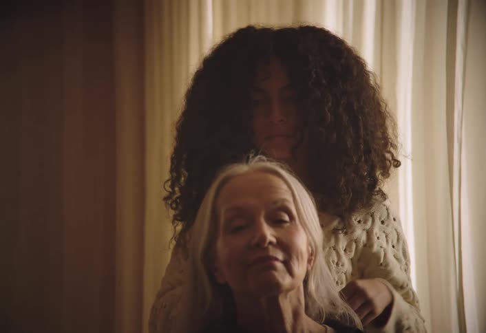 Girl with curly hair combs the hair of a seated woman
