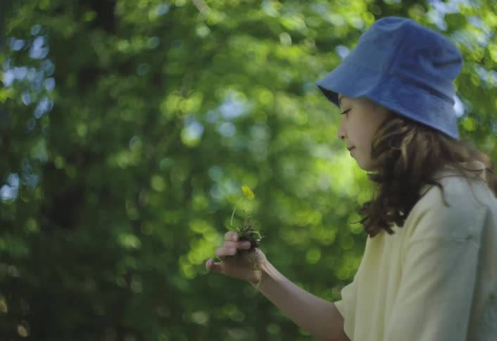 A little girl digs a dandelion out of the grass with a hand trowel