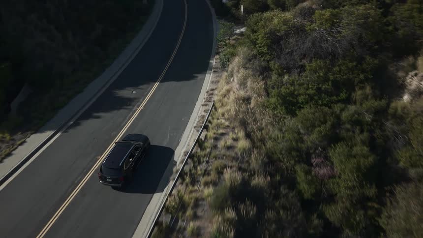 An suv driving up a road between tree covered hills