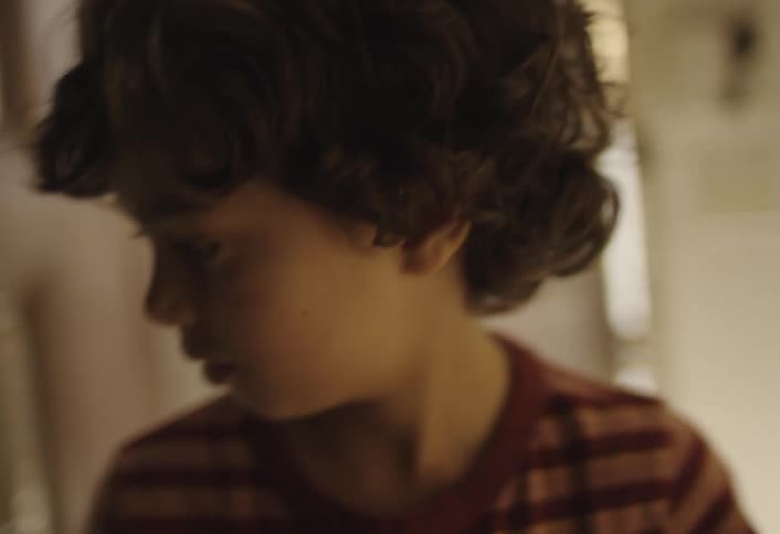 A young person with curly hair wearing a striped shirt is seen in a room with a washing machine folding laundry they carefully fold a white towel and then a striped piece of clothing before placing them aside