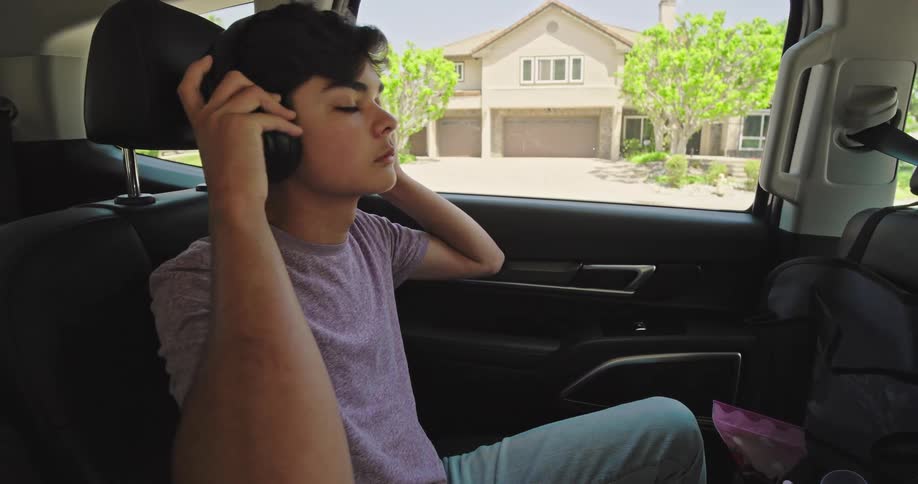 The teenager puts on headphones in the back seat of the car