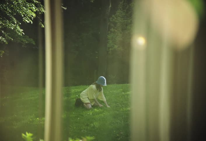 A girl wearing a blue hat is digging the lawn using a gardening spade