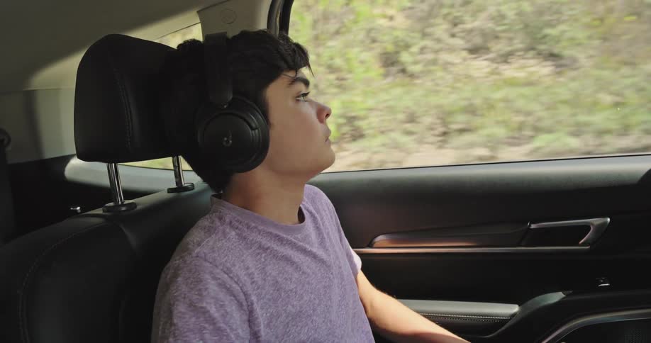 Boy putting on headphones while sitting in the back seat of a moving vehicle