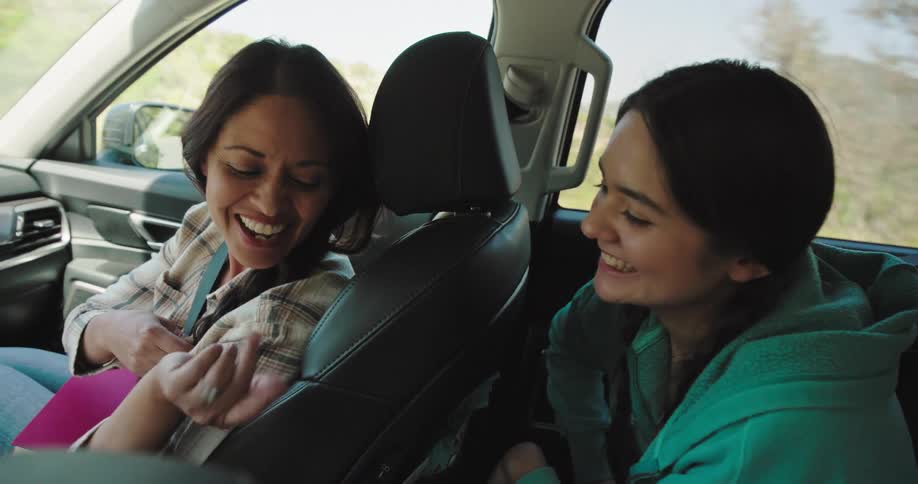 A daughter braids her mothers hair on a road trip