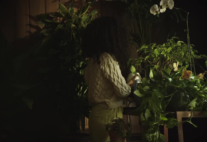 Curlyhaired person with a teapot watering flowers in an indoor space