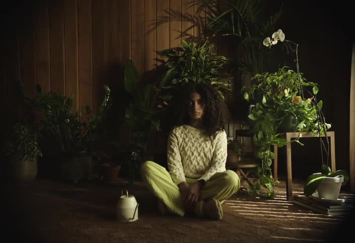 Curly haired girl sitting in a room with plants in an indoor space