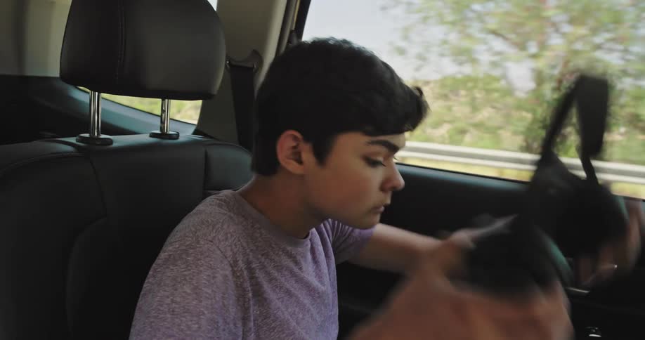 Boy taking off his headphones while sitting in the backseat of a moving car