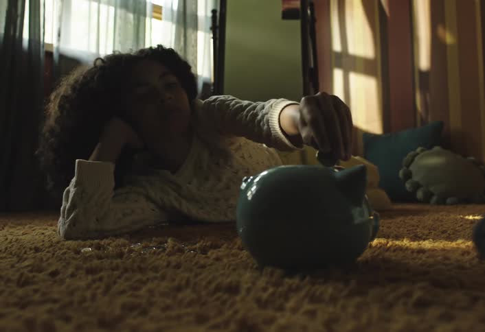 Girl lying on the carpet and putting coins into a piggy bank