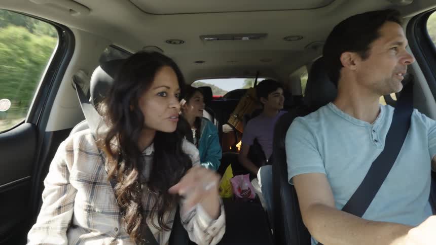 A family are talking and pointing in the car on a road trip