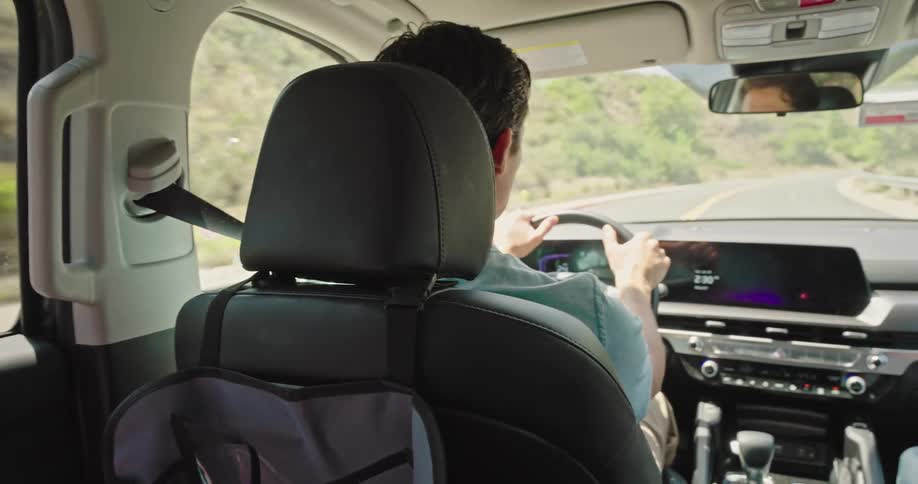 A person is sitting in the back seat of a car with their head resting against the seat the camera pans across to show the driver a man looking ahead at the road