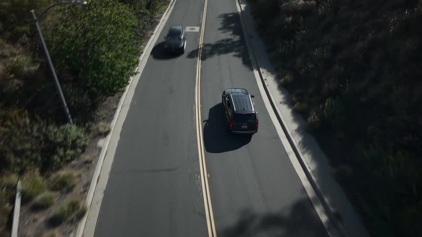 Black suv traveling on a paved road in an environment surrounded by mountains