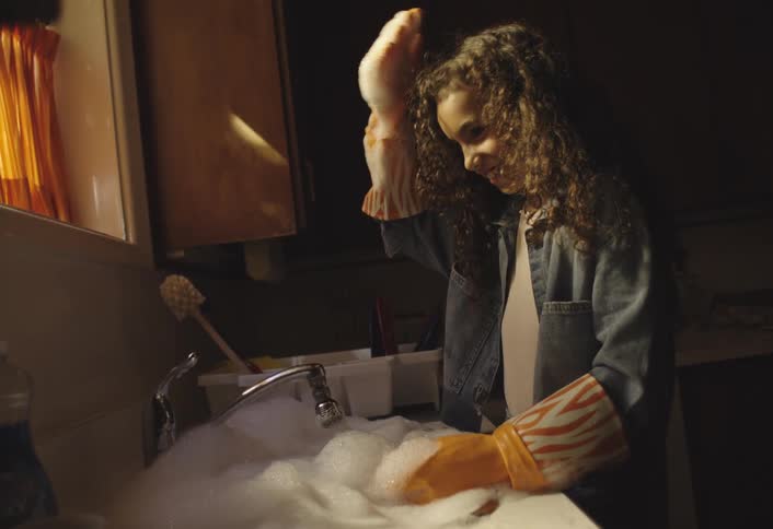 Young girl having fun blowing with the bubbles while washing dishes