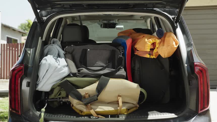 Family storing suitcases and utensils in the trunk of a car