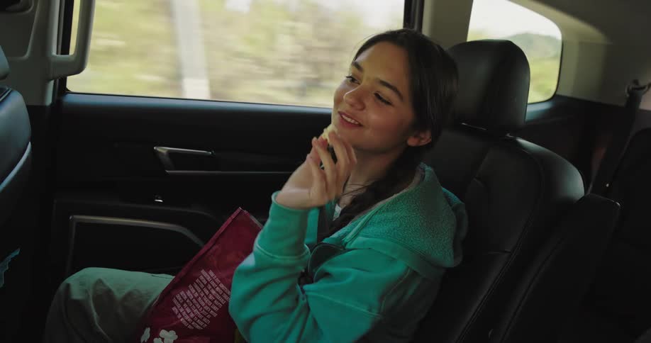 Girl eating snacks while sitting in a moving car with her mother interacting happily