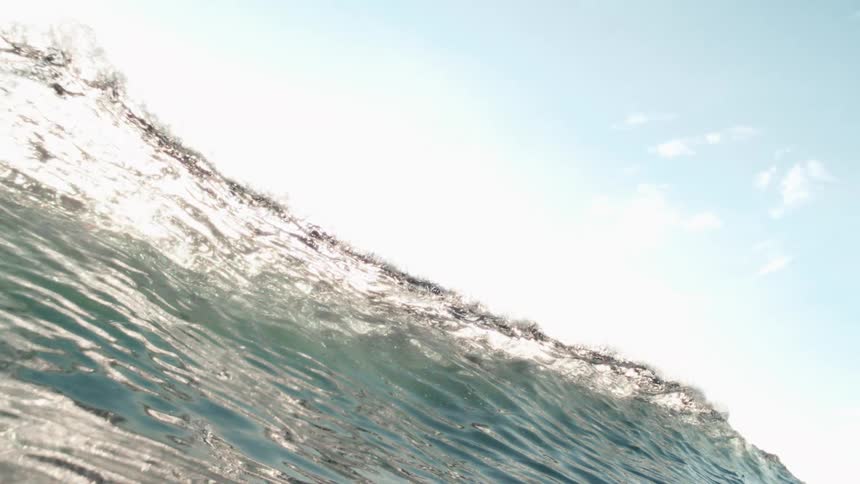 Wave bends powerfully and brilliantly in the sunlight reflecting bright hues of blue and white against a clear sky