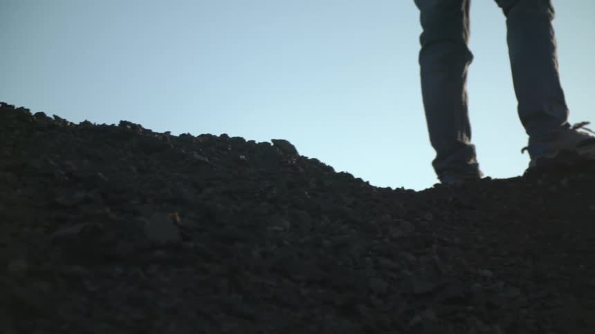 A hiker climbs up and stands on top of a rock hill