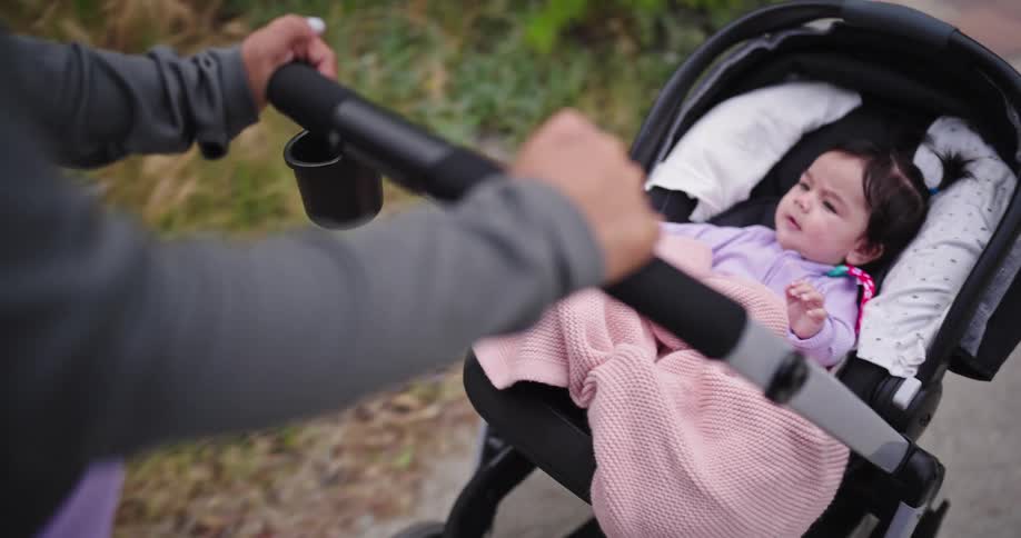 Mother pushes her daughter in a baby carriage along a sidewalk