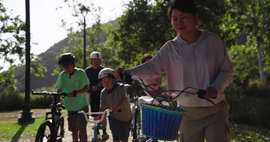Family walks their bicycles along a park path near a green hill