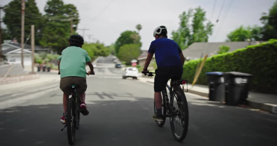 Father and son pedal along a sloping road through a residential neighborhood