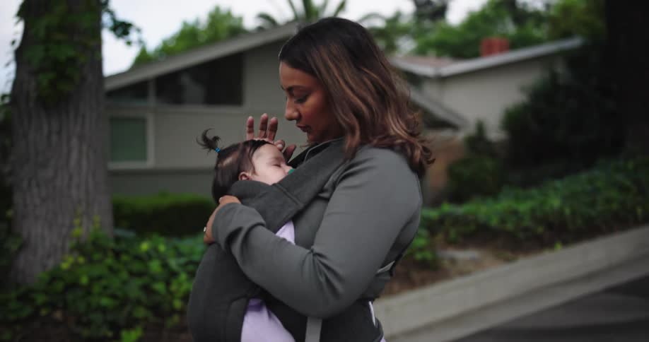 Mother carrying her sleeping baby in a baby carrier on a walk through a neighborhood