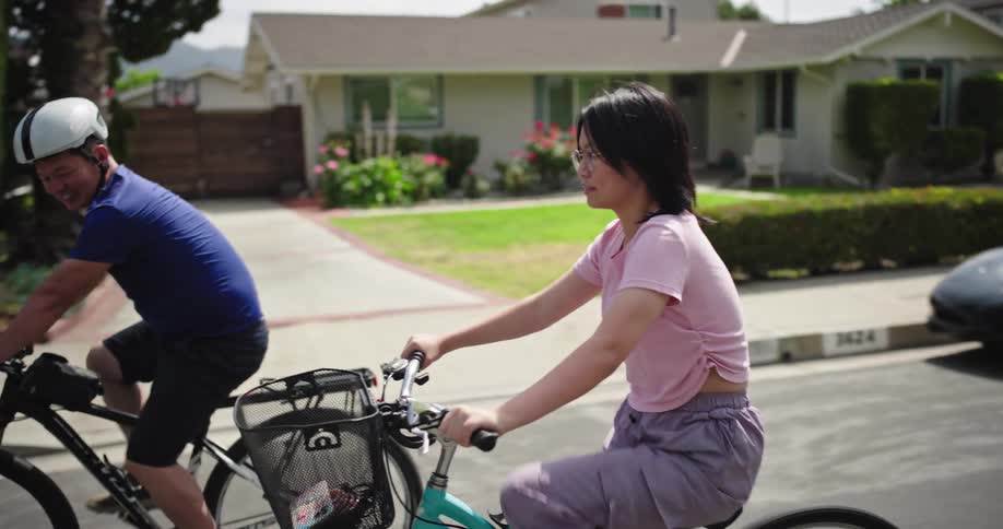 A man and a girl are riding bicycles side by side on a suburban street on a sunny day
