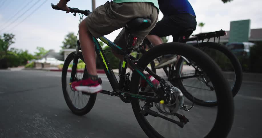 A closeup of two cyclists in motion shows legs pedaling and tires spinning on a paved road