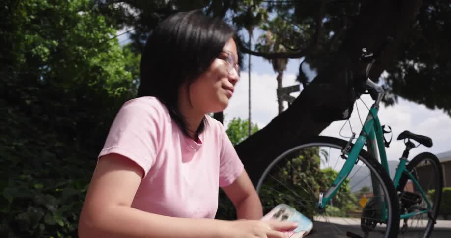 A woman in a pink shirt gets on a bicycle with a front basket along a quiet suburban street