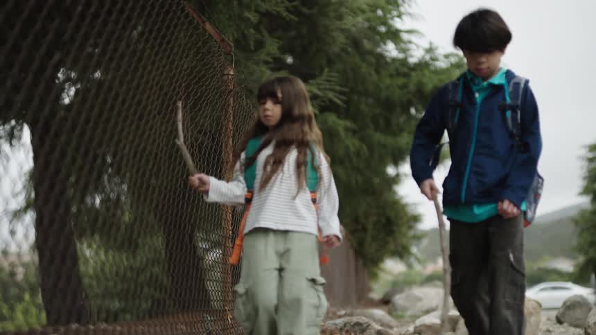 Two kids walk outside with sticks