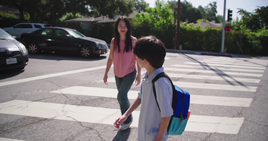 People walk across a residential street at the crosswalk on a summer day