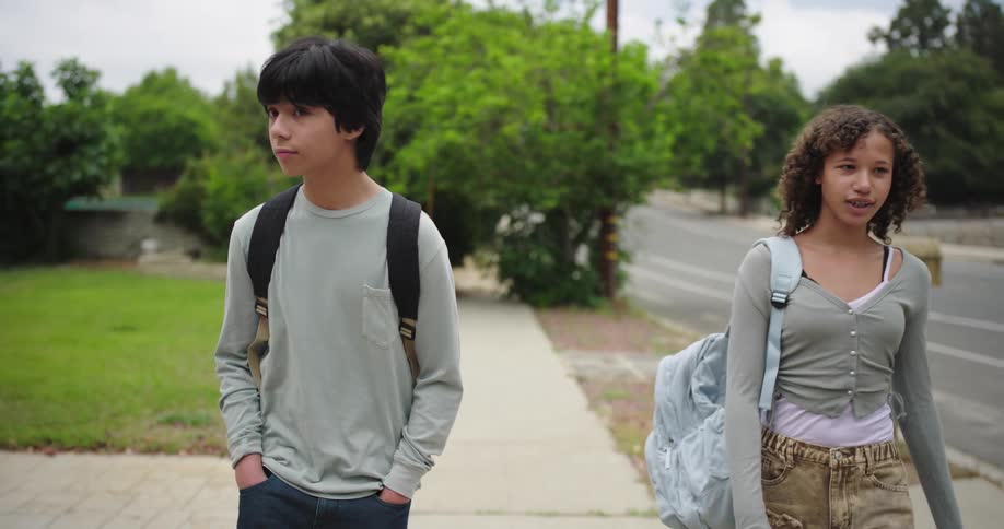 Two teenagers walking side by side on a sidewalk without making eye contact