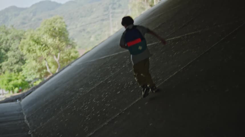 The video shows a child with a blue and orange backpack walking through a dimly lit underpass towards the bright outdoors at one point the child briefly runs up the side wall of the underpass