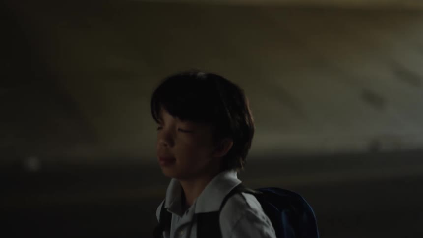 The video features a child with a dark backpack seen from the side with dark hair the setting appears to be a dimly lit tunnel or underpass suggested by the low light and concrete background