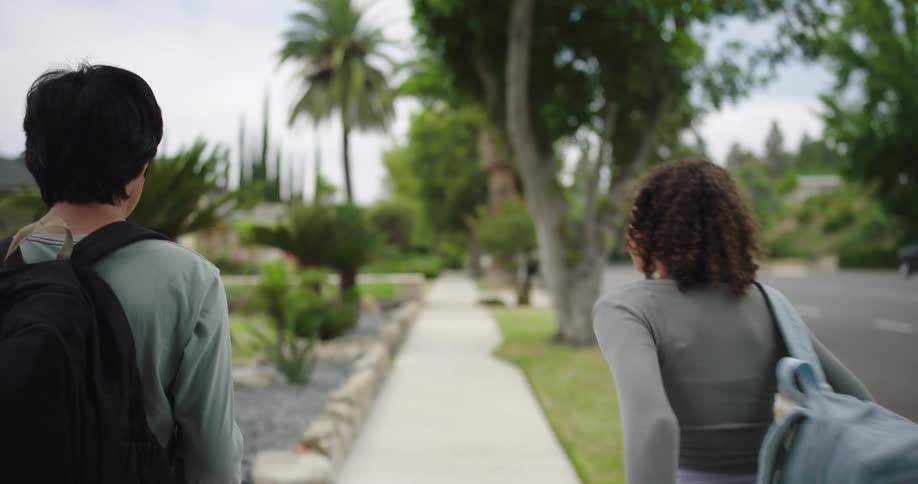 Two teenagers with backpacks walking on a suburban sidewalk
